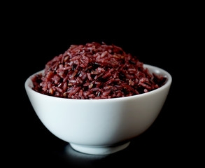 The brown rice berry in the white bowl isolated on black background