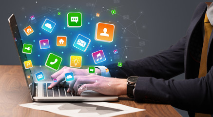 Businessman hand typing on laptop with flying application icons around