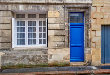 Blue door and white window of an old stone building in Bordeaux