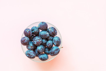 Bowl with plums on a pink background, top view, copy space.