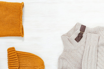 Female autumn clothing, warm knitted scarf and cap orange colored and light woolen pullover. Shopping overview concept with copy space. Top view. Flat lay.