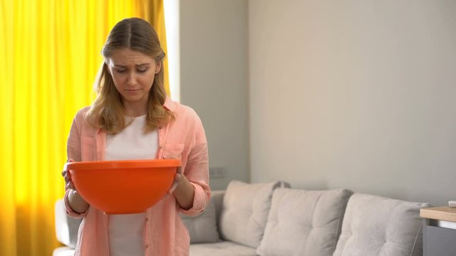 Upset woman holding pot while water leaking from ceiling, house needs renovation