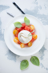 Salad with burrata cheese, watermelon and yellow tomatoes. Flatlay on a white concrete background, studio shot