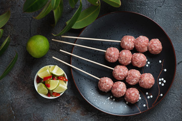 Black plate with raw vietnamese nem nuong skewers ready to be cooked, top view over dark grey stone background