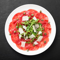 Beef Carpaccio cold appetizer with parmesan, capers and arugula on white plate.Top view.
