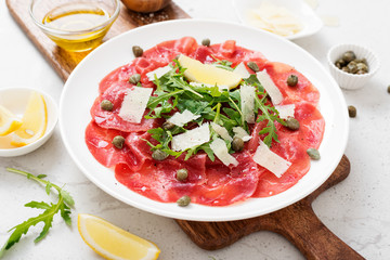 Beef Carpaccio cold appetizer with parmesan, capers and arugula on white plate.