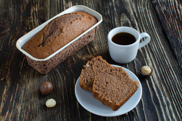 Coffee cake with macadamia nuts and cup of coffee on dark wooden background