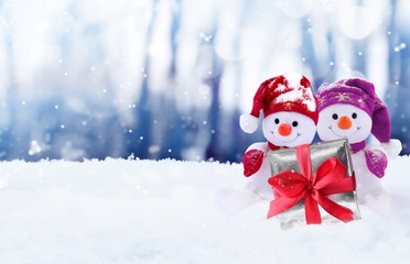 Naklejka na ściany i meble Funny two snowmen with gift box in the winter scenery. Christmas decoration