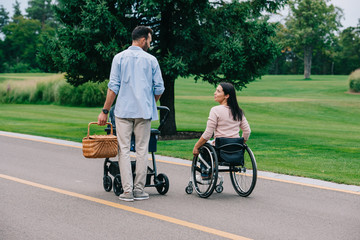 happy disabled woman looking at husband carrying straw basket while walking in park with baby...