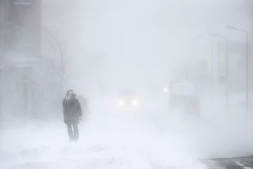 Fotobehang Snowstorm in the city. A man during a blizzard is walking along the street. Cars on a snowy road. Strong wind and snowfall. Arctic climate. Extreme North. Anadyr, Chukotka, Siberia, Far East Russia. © Andrei Stepanov