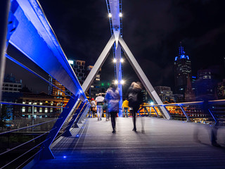 Unrecognisable people crossing the bridge over the Yarra river in Melbourne in winter.