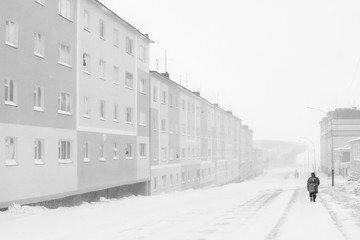 Winter in the city. The street is covered in snow. A man is walking along the sidewalk. Cold winter weather. A town in the Arctic. Anadyr, Chukotka, Siberia, Far East Russia. Black and white photo.