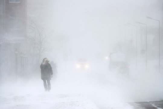 Snowstorm in the city. A man during a blizzard is walking along the street. Cars on a snowy road. Strong wind and snowfall. Arctic climate. Extreme North. Anadyr, Chukotka, Siberia, Far East Russia.