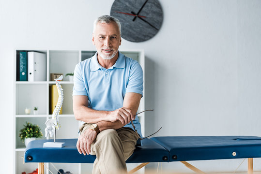 cheerful man sitting on massage table and holding glasses - Powered by Adobe
