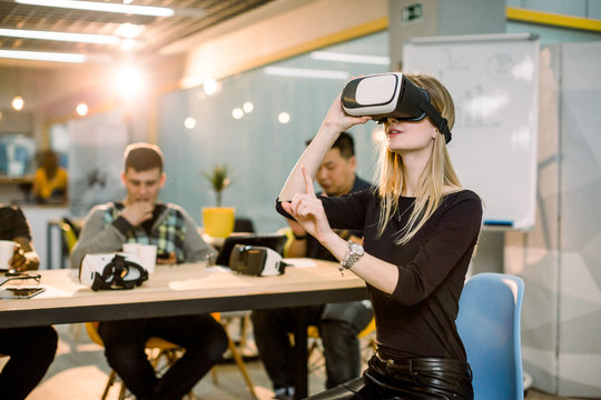 Business team of multiethnical people working on virtual reality applications and games, young excited woman testing VR glasses or goggles sitting in the office room with coworkers