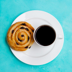 Fresh danish pastry with raisins with a cup of black coffee on blue table background. Top view.