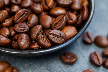 Obraz premium Coffee beans close up shot in black bowl on grey slate background. Close up.