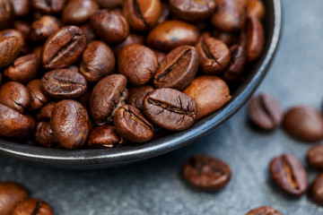 Coffee beans close up shot in black bowl on grey slate background. Close up.