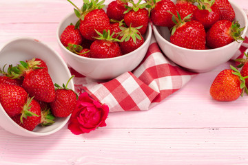 Bowl of strawberry harvest on wooden table close up