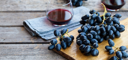 Glass of red wine with fresh grape on wooden table. Close up.
