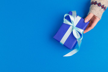Small gift box in female hands on blue background, view from above