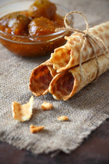 Waffle rolls and scattered broken pieces tied with rope and Fig jam in a glass bowl on burlap and on dark countertop. Vertical frame.