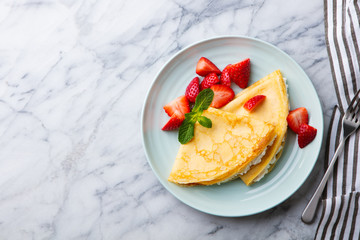 Crepes, thin pancakes with cream cheese, ricotta and fresh strawberries. Marble background. Top...