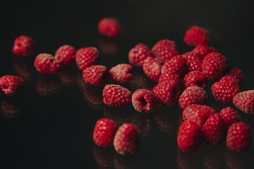 berries of red raspberries in a bunch lie on a black glass top view. sweet summer berries