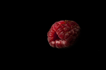 one berry of red raspberries lies isolated on a black background top view close-up. sweet summer berries close-up