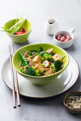 Soba noodles with vegetables and fried tofu in a bowl. Grey background.