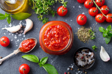Tomato sauce in a glass jar with fresh herbs, tomatoes and olive oil. Top view. Slate background.