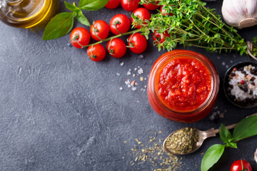 Traditional tomato sauce in a glass jar with fresh herbs, tomatoes and olive oil. Top view. Copy space.