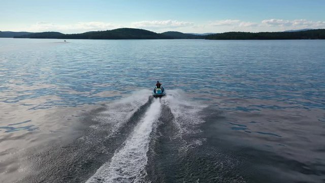 Aerial video following fast jet ski on lake during summer with blue ski
