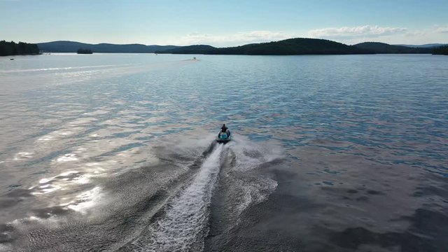 Jet ski racing off into distance on lake during summer, cinematic aerial video