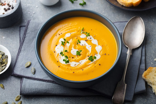 Pumpkin, carrot cream soup in a bowl. Grey background.