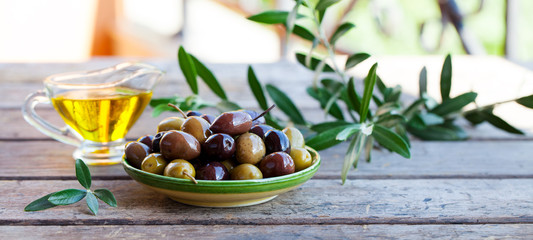 Assortment of fresh olives and olive oil in glass jug on wooden background. Copy space.