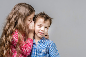 Girl in a red blouse whispers in the ear of a boy in a blue shirt. © R