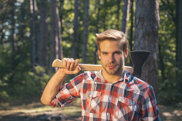Obraz premium Lumberjack carries axe on shoulder. Deforestation. Handsome man with axe. Lumberjack in the woods with an ax.