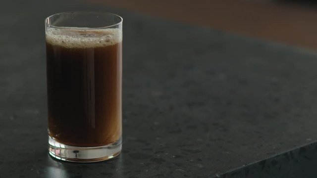 Slow motion nitro coffee in glass on terrazzo surface