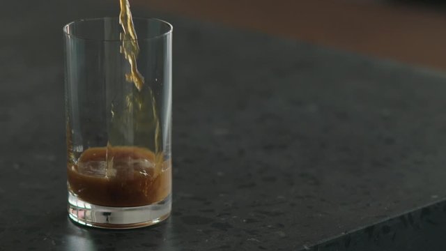 Slow motion pour nitro coffee into glass on terrazzo surface