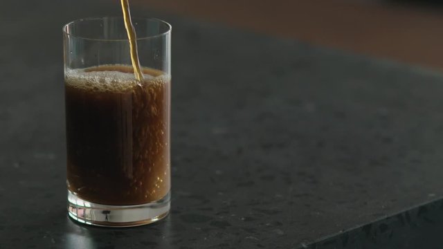 Slow motion pour nitro coffee into glass on terrazzo surface