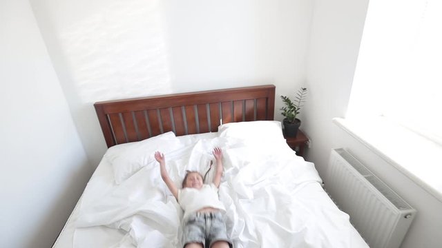 Child jumping in the bedroom on the white bed wearing white clothes