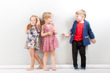 Fototapeta premium Two little girls and a boy against the background of a white wall.