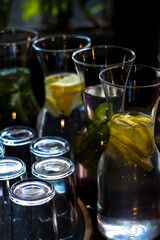 Beautiful glass pitchers with mint, water and fruits. Dishes in the café. Dark background. Cups and glasses.