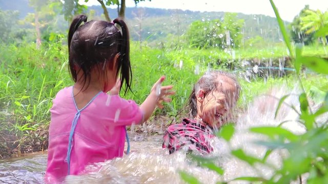 Children playing  barefoot in stream water, play mud and sand.