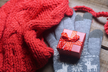 Red gift box on gray glove near red yarn winter hat with background wood table.