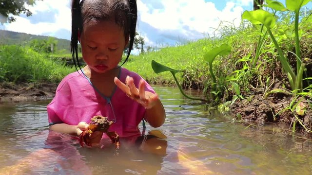 Children playing  barefoot in stream water, play mud and sand.