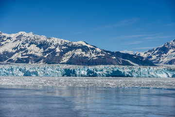 Naklejka na ściany i meble Hubbard Glacier in the sunshine with icebergs floating in the water. 