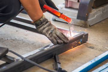 The skill worker use the electric welding machine welding the metal tube structure for assembly  the metal frame. The construction worker build the metal frame by electric welding machine.