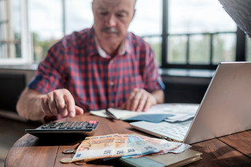 Serious mature hispanic man man checking home finance calculating money. Focus on euro money.
